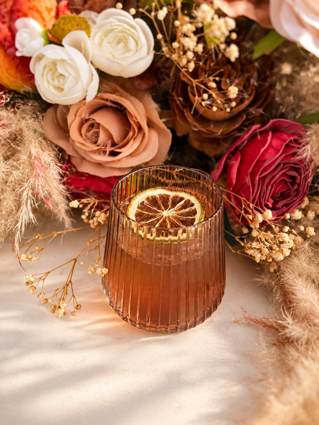 Cocktail garnished with dried citrus beside warm floral decorations