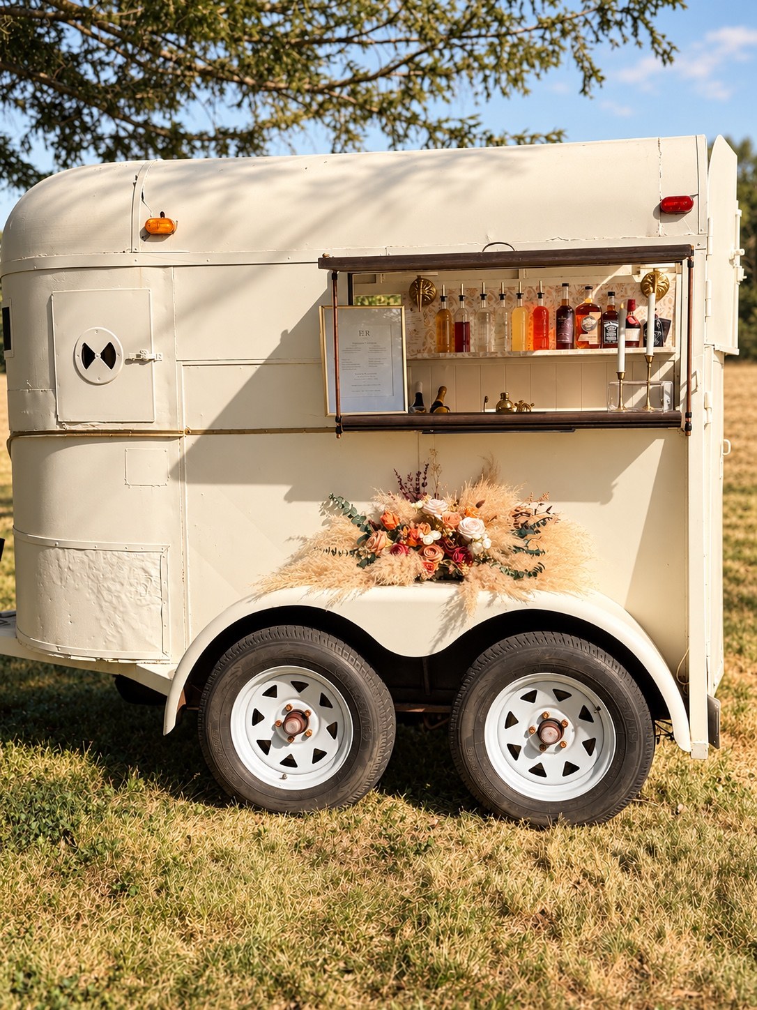 The Willow's cream vintage mobile bar trailer decorated with flowers at an outdoor event